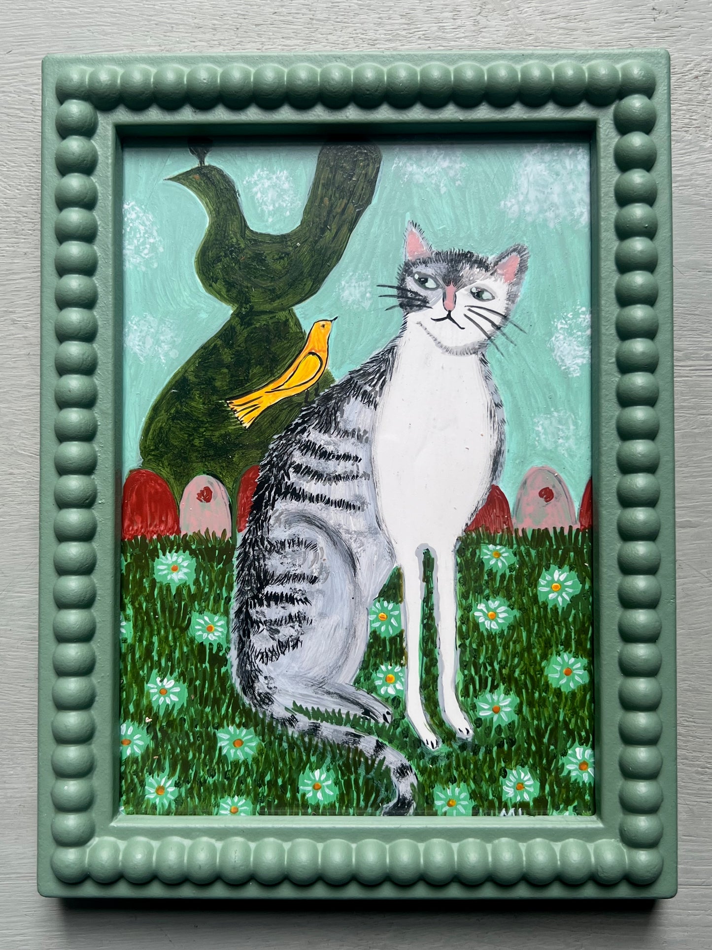 Original acrylic painting of a grey tabby cat sitting amongst white daisies beside a yellow bird and dark green ornamental figure against a pale turquoise background, painted on a 5 x 7 inch wooden board.